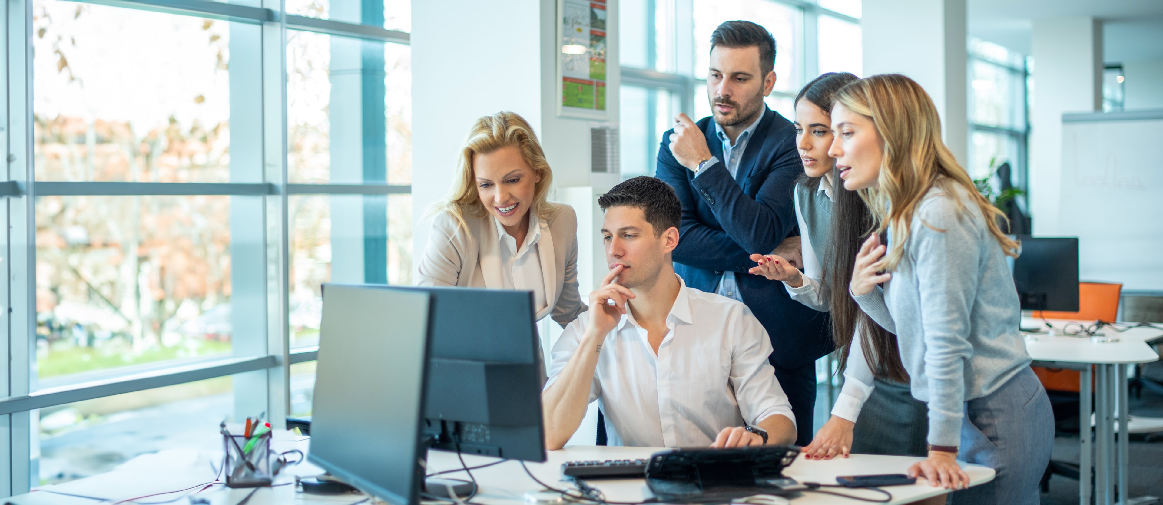 Business team gathered around a computer collaborating in a modern office