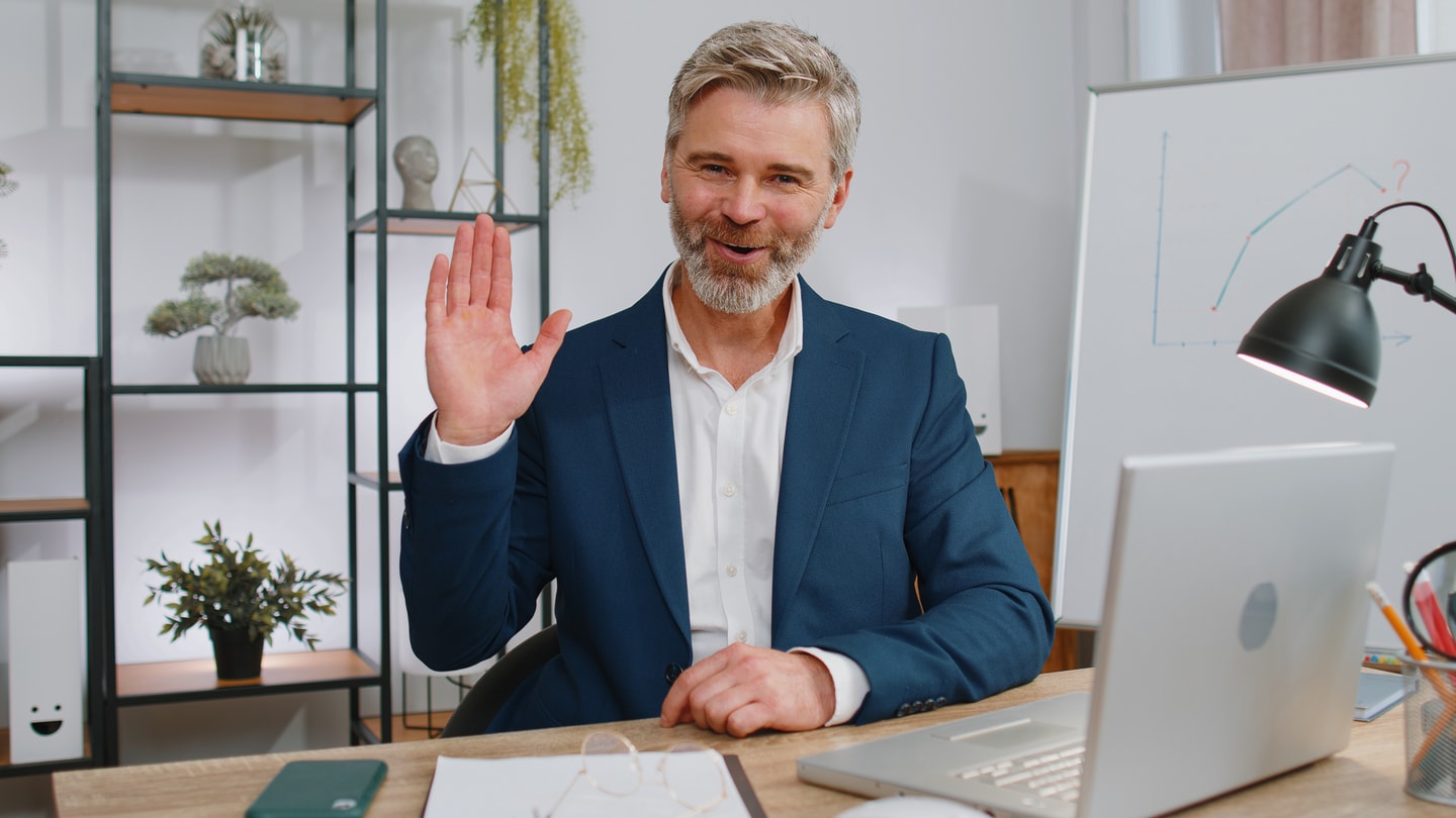 Businessman smiling and waving during a video call from his office